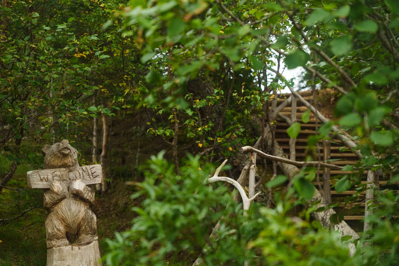 Hand-carved wooden bear holding a WELCOME sign at the entrance to camp