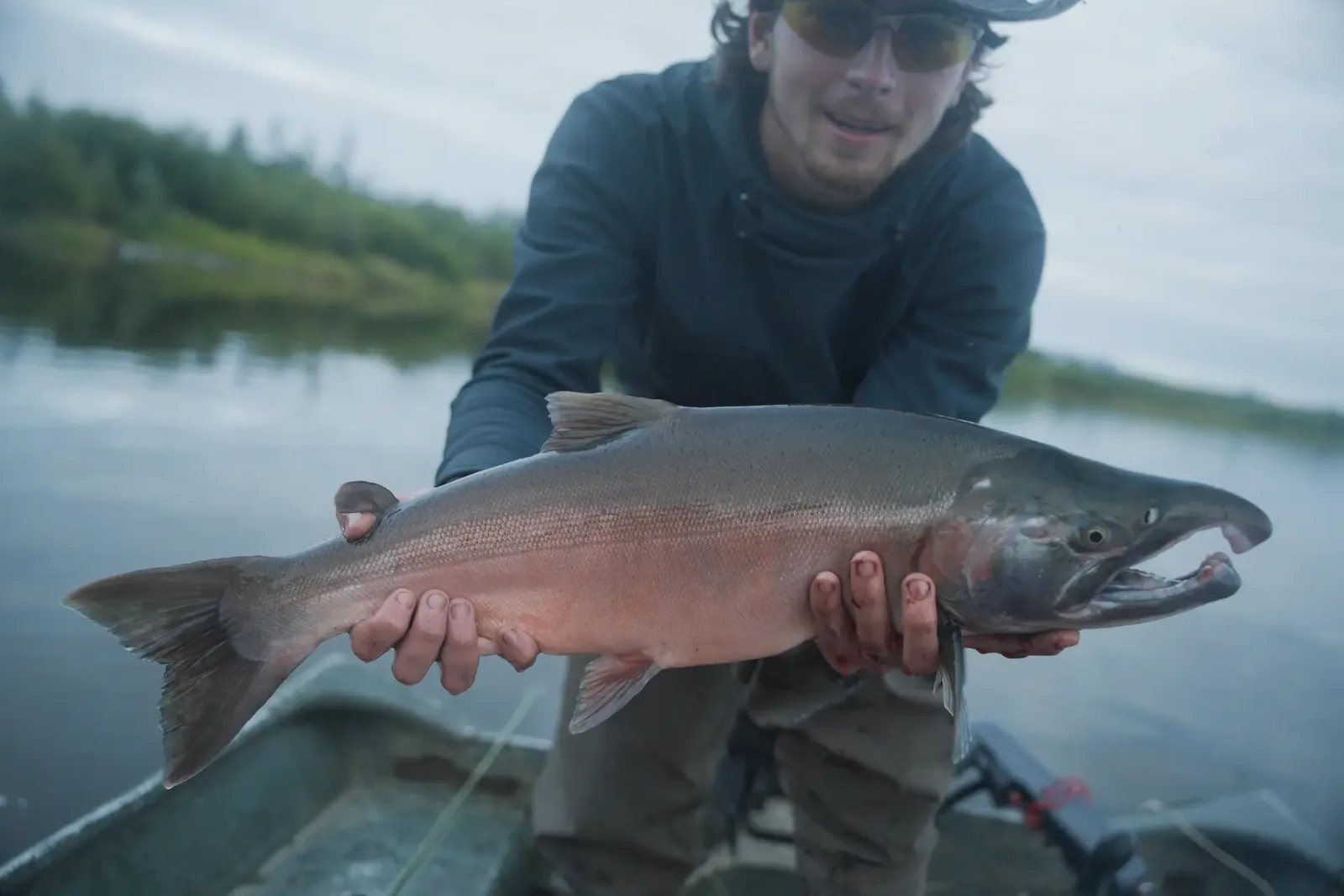 Angler presenting a freshly caught coho salmon from a river boat