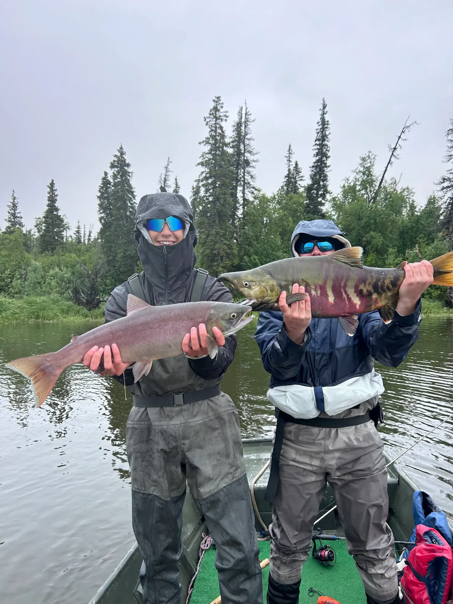 Two anglers in rain gear holding a large chum salmon and a silver salmon on the boat