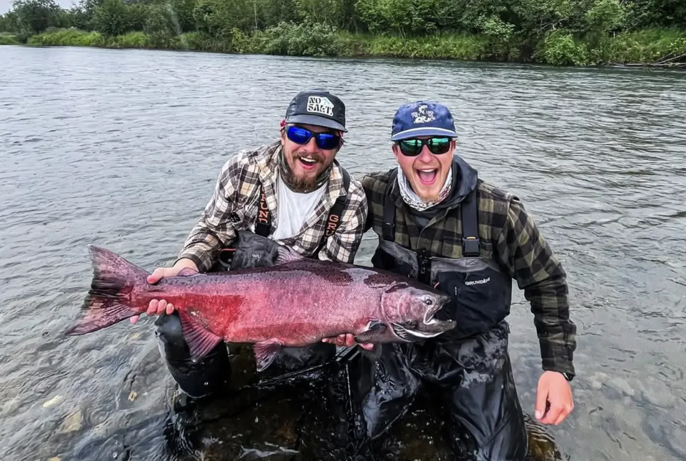 Two excited anglers kneeling in the river holding a huge red king salmon