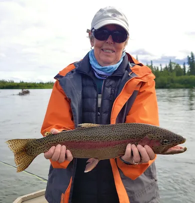 Angler in an orange jacket holding a rainbow trout aboard the boat on the Mulchatna River